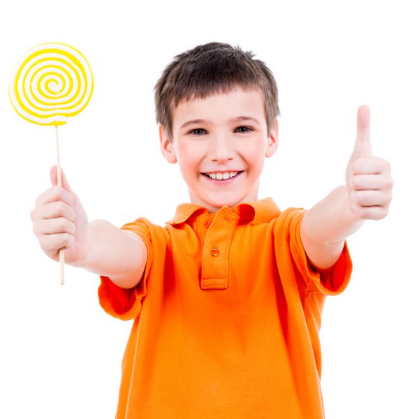 پسر شاد با تی شرت نارنجی با آب نبات رنگی که علامت شست را نشان می دهد - جدا شده روی سفید