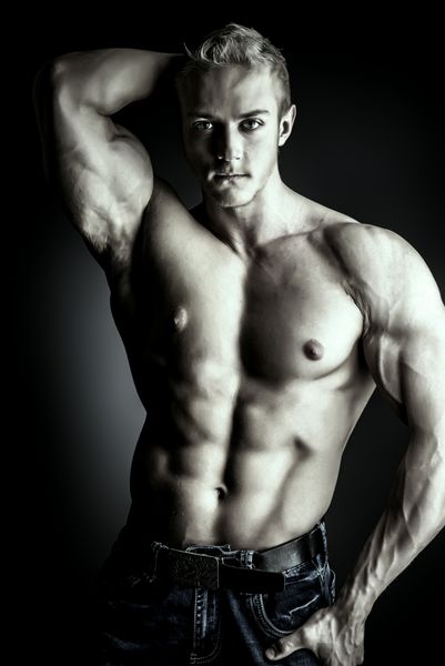 مرد بدنساز عضلانی که روی پس زمینه تیره ژست گرفته است زیبایی مردانه ورزش ها