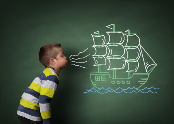 کودک در حال دمیدن یک نقاشی از یک قایق بادبانی با گچ بر روی یک مفهوم تخته سیاه برای آرزوها رویاها امیدها و آرزوها
