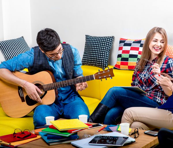 مرد جوان و خوش تیپ یک گیتار برای دوست دختران روی مبل زرد در خانه