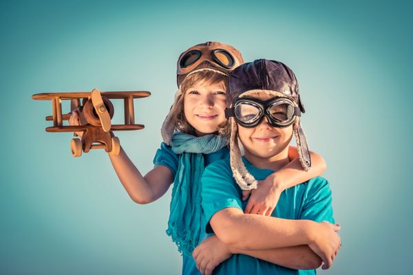 بچه های شاد با هواپیمای چوبی قدیمی در فضای باز پرتره کودکان در پس زمینه آسمان تابستان مفهوم سفر و آزادی رترو تن