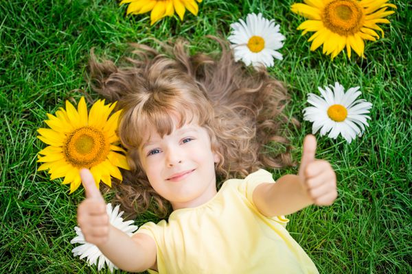 کودک شادی که روی چمن دراز کشیده است بچه بامزه در پارک گل های زیبای بهاری unus نمای بالا پرتره موفقیت و برنده شست بالا پسندیدن