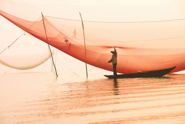 ماهیگیر ناشناس تورهای خود را در اوایل صبح در رودخانه ای در هویان ویتنام چک می کند