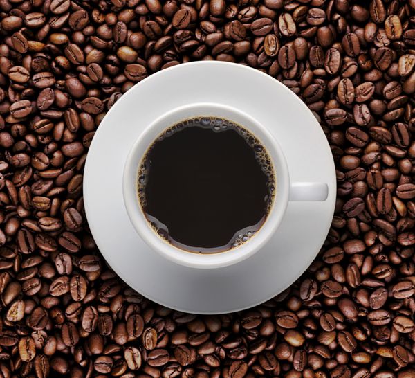 نمای چشم پرنده از فنجان قهوه روی دانه های قهوه خام نمای بالای فنجان قهوه روی دانه قهوه بو داده