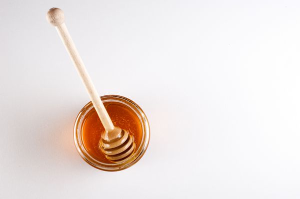 شیشه ای پر از عسل و چوب چوبی در آن