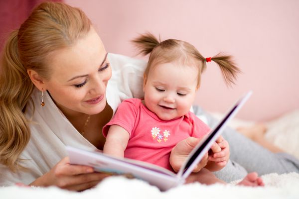 مادر خوشحال در خانه برای دختر بچه کتاب می خواند
