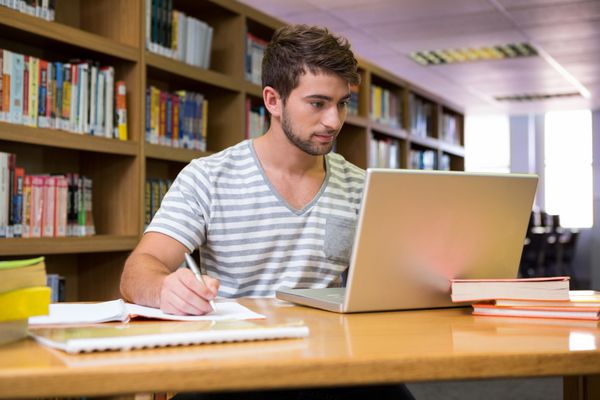 دانشجو در حال تحصیل در کتابخانه با لپ تاپ در دانشگاه