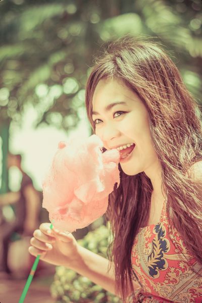 دختر ناز آسیایی تایلندی در حال خوردن آب نبات صورتی با شادی در تابستان روشن در طبیعت نسخه مفهومی پس زمینه سبز در رنگ پرنعمت