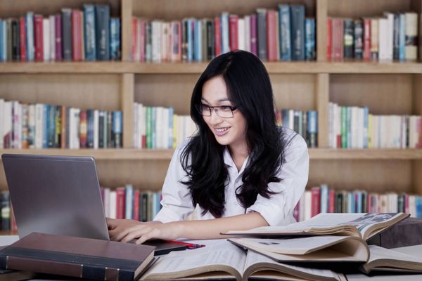پرتره دانش آموز باهوش در حال مطالعه در کتابخانه و استفاده از کامپیوتر لپ تاپ