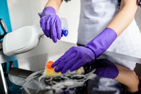 دست های زن در حال تمیز کردن بالای آشپزخانه در دستکش های محافظ لاستیکی