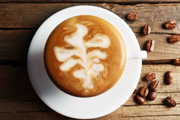 فنجان قهوه لاته آرت با دانه های روی میز چوبی نمای بالا