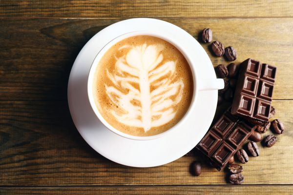 فنجان قهوه لاته آرت با دانه ها و شکلات در زمینه چوبی