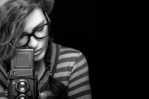 از نزدیک زن جوان جذاب با لباس شیک و با استفاده از دوربین قدیمی عکس می گیرد پرتره سیاه و سفید جدا شده روی پس زمینه سیاه با کپی sp برای متن
