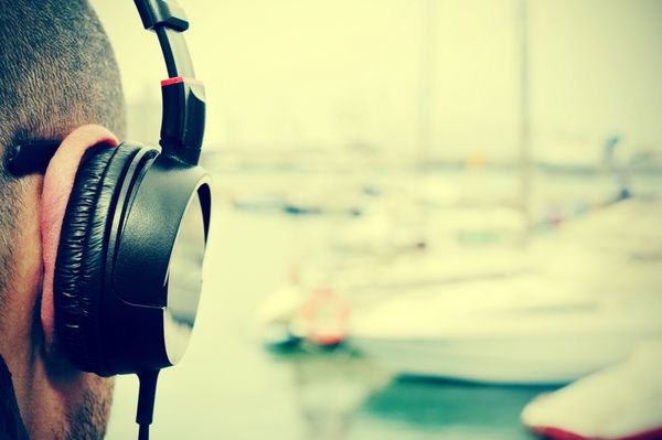 نمای نزدیک از یک مرد جوان در حال گوش دادن به موسیقی با هدفون در مقابل دریا در یک تفرجگاه دریایی با جلوه فیلتر