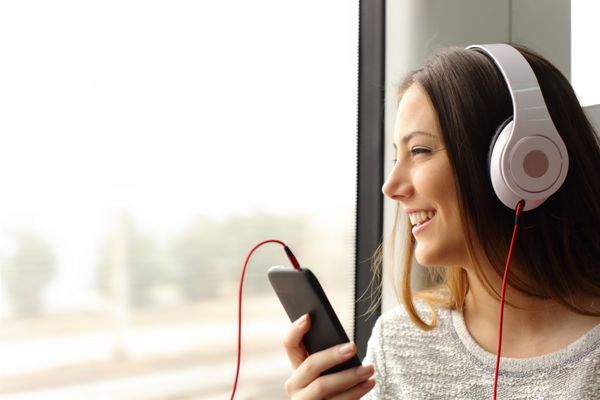 مسافر نوجوان خوشحال در حال گوش دادن به موسیقی که در قطار سفر می کند و از پنجره نگاه می کند