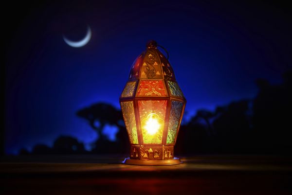 فانوس رمضان رنگارنگ روشن در مقابل آسمان آبی شب با هلال ماه