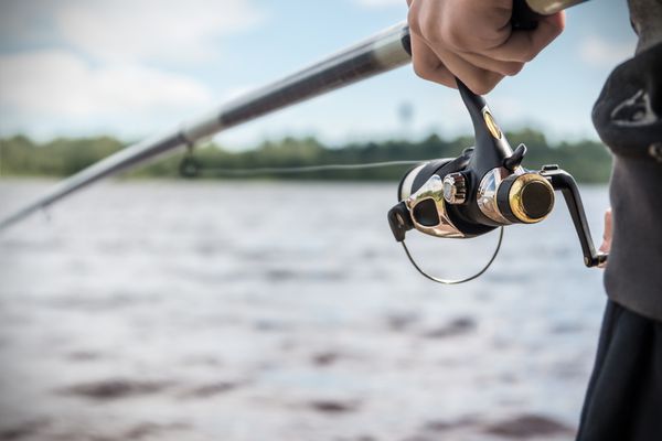 دستی که چوب ماهیگیری را با قرقره گرفته است روی قرقره های ماهیگیری تمرکز کنید