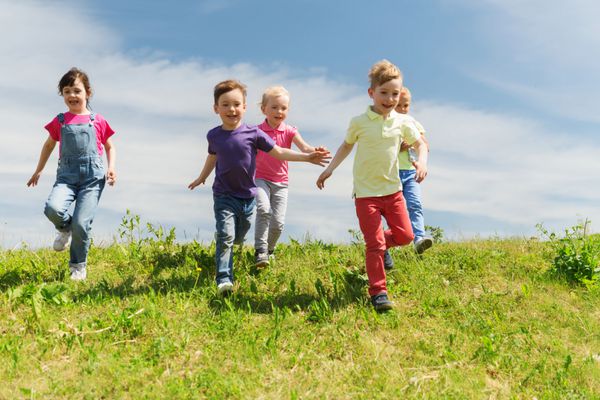 تابستان کودکی اوقات فراغت و مفهوم مردم - گروهی از بچه های شاد تگ بازی و دویدن در زمین سبز در فضای باز