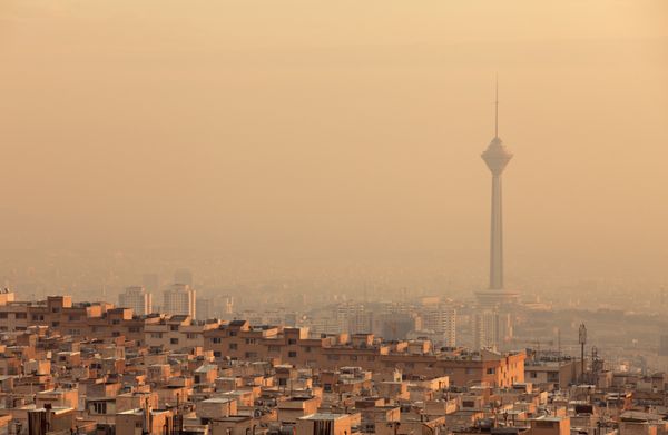 ساختمان‌های مسکونی روبروی برج میلاد در خط افق آلوده هوای تهران که با غروب طلایی خورشید روشن شده است