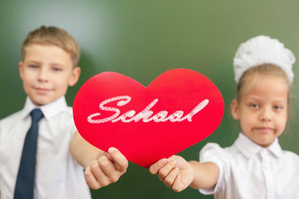 بچه های شاد مدرسه یا بچه هایی که نماد قلب را در کلاس مدرسه نزدیک تخته سیاه در دست دارند آموزش عشق به مدرسه به کودکان بسیار مهم است به مدرسه خوش آمدید