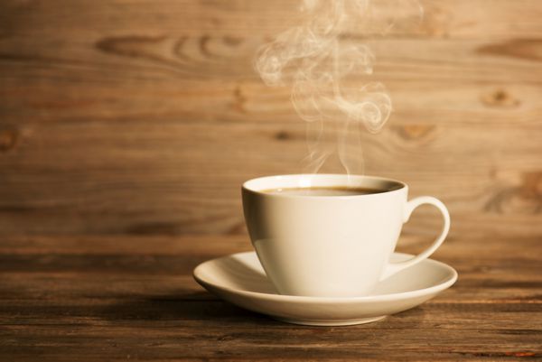 بخارپز کردن قهوه در لیوان و نعلبکی سفید در تنظیم فوکوس ملایم با نور محیطی چشمگیر روی پس زمینه چوبی تیره