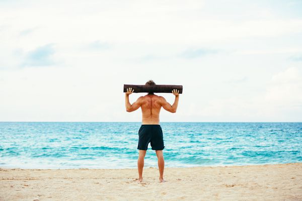 تمرین ساحلی ورزشکار مرد در حال ورزش در فضای باز در ساحل با کنده درخت تناسب اندام و سبک زندگی سالم