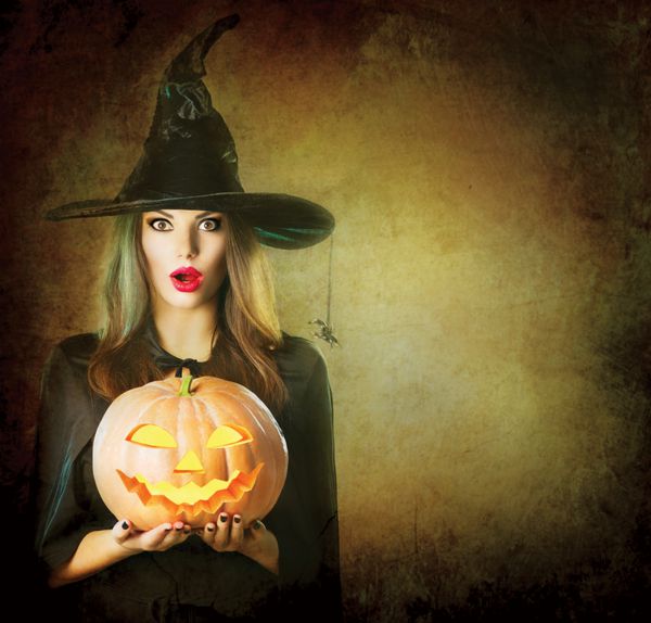 هالووین جادوگر را با کدو تنبل جادویی شگفت زده کرد زن جوان زیبا با کلاه و لباس جادوگر که کدو تنبل حکاکی شده فانوس جک را در دست دارد طراحی هنری هالووین