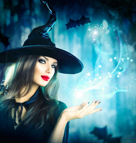 جادوگر هالووین با جادو در یک جنگل تاریک زن جوان زیبا با کلاه و لباس جادوگر که نور جادویی را در دست دارد طراحی هنری هالووین