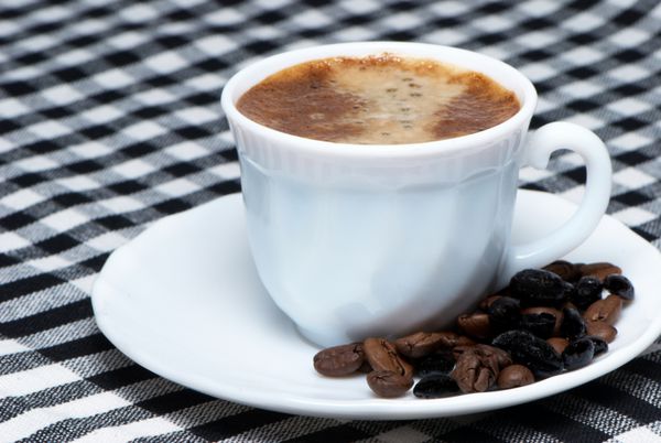 نمای نزدیک فنجان قهوه روی دانه های قهوه بو داده تیره
