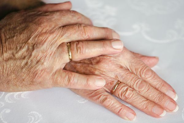 دو دست یک زن و شوهر پیر روی هم دراز کشیده اند با حلقه های ازدواج طلایی