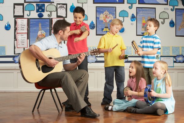 معلم مرد گیتار با دانش آموزانی که در کلاس درس موسیقی دارند