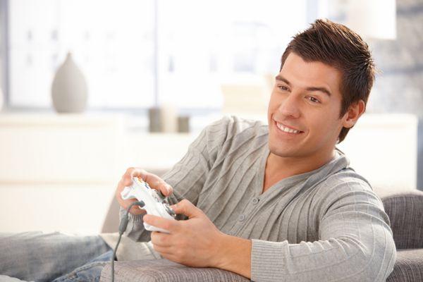 پسر جوان در حال لذت بردن از بازی کامپیوتری با جوی استیک با خوشحالی لبخند می زند