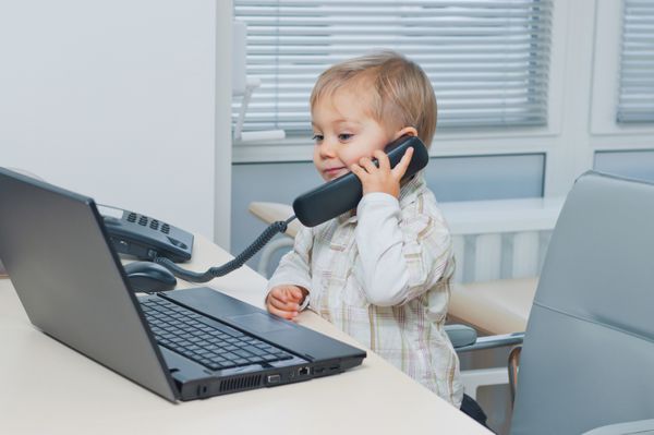 پسر کوچک تجاری ناز با تلفن و کامپیوتر در دفتر