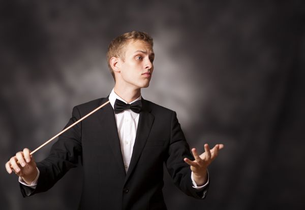 پرتره یک رهبر ارکستر جوان که با باتوم خود در یک کنسرت کلاسیک کارگردانی می کند