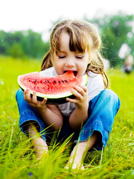 دختر بچه ناز در حال خوردن هندوانه روی چمن در تابستان