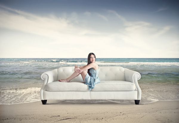زن زیبا روی مبل در ساحل نشسته است