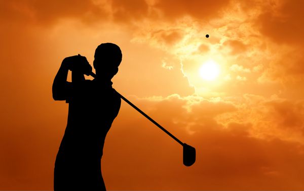 مرد بازیکن گلف در هنگام غروب خورشید توپ به هوا را به تصویر می کشد