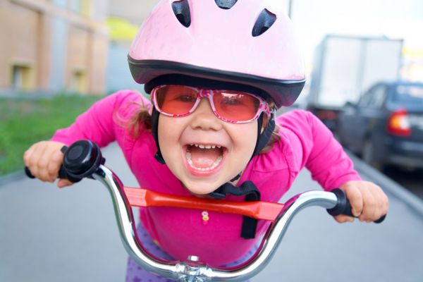 پرتره یک دختر بامزه بازیگوش با کلاه ایمنی صورتی روی دوچرخه اش