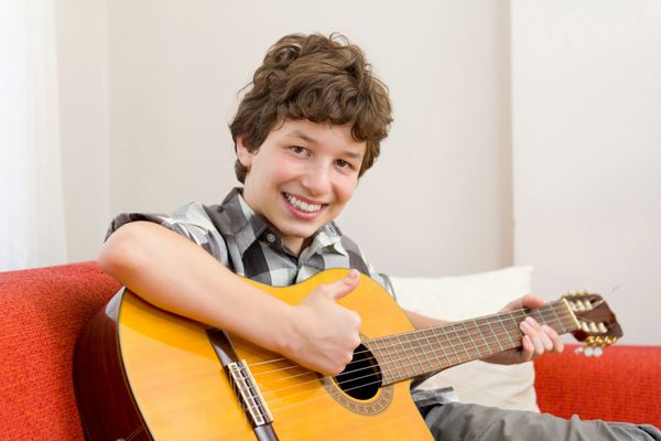 پسری در سنین پایین که در حالی که گیتار خود را در دست گرفته و روی کاناپه نارنجی رنگی نشسته است انگشت شست را بالا می‌آورد و لبخند شادی می‌زند