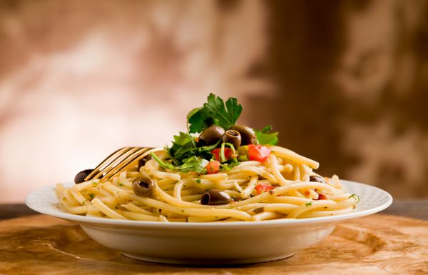غذای خوشمزه گیاهی از پاستا با زیتون و جعفری روی میز چوبی