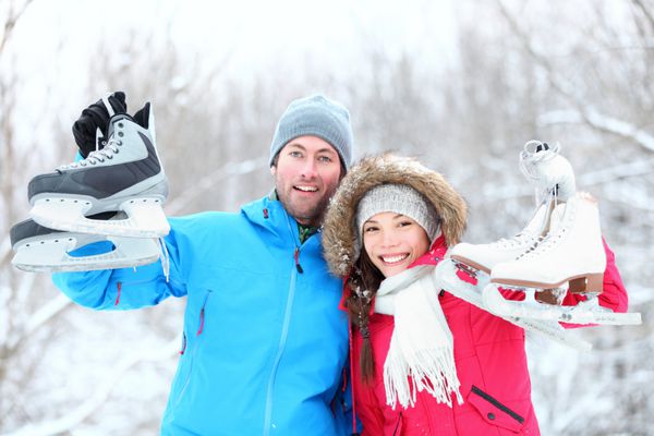 زوج زمستانی اسکیت روی یخ لبخند می زنند و خوشحال و هیجان زده هستند و اسکیت های روی یخ را در فضای باز در برف نشان می دهند مفهوم سبک زندگی سالم زوج چند نژادی جوان زیبا