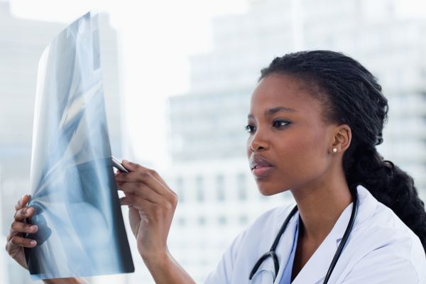 پزشک زن متمرکزی که به مجموعه ای از اشعه ایکس در مطب خود نگاه می کند