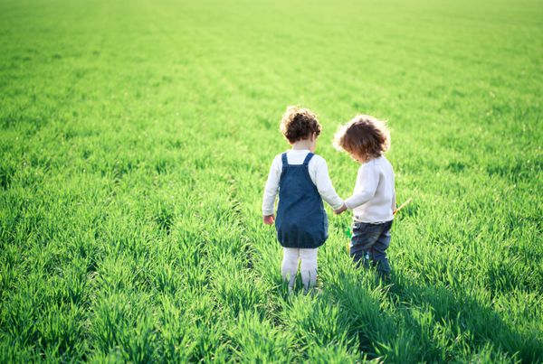 دو کودک که در زمین سبز بهاری می روند
