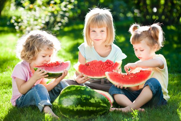 گروهی از کودکان شاد در حال خوردن هندوانه در فضای باز در پارک بهار