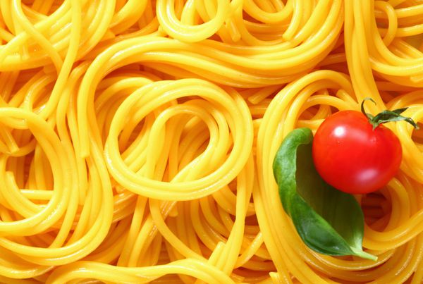 نمای نزدیک از اسپاگتی تازه آب پز شده در الگوهای تصادفی برای یک پس زمینه جالب با ریحان و گوجه فرنگی