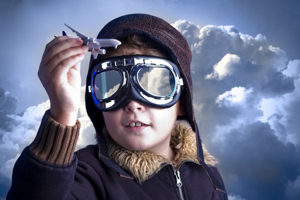 پسر کوچک در کلاه خلبان پسری به عنوان یک خلبان قدیمی که یک هواپیمای اسباب بازی در دست دارد