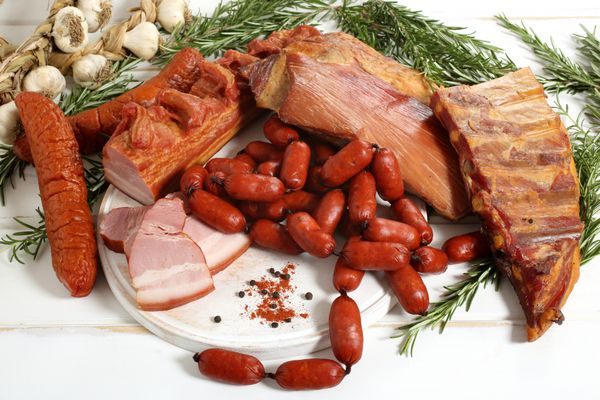 سوسیس گوشت دودی خوشمزه و بیکن روی میز چوبی سفید