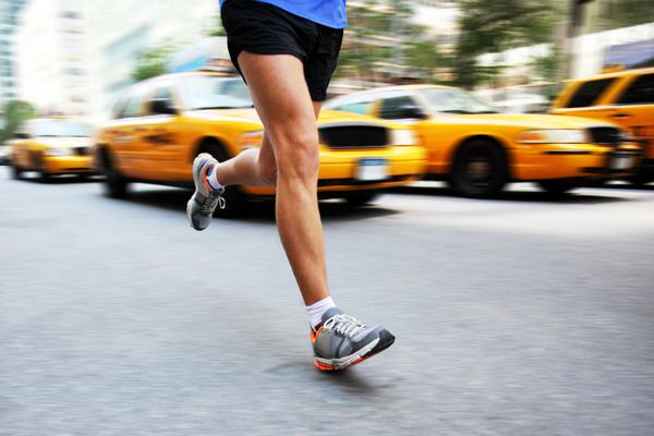 دویدن در شهر نیویورک - مرد دونده شهری در حال دویدن در خیابان منهتن با خودروهای تاکسی زرد رنگ و ترافیک تصویر سبک زندگی شهری از تمرین دویدن مرد در مرکز شهر پاها و کفش های دویدن