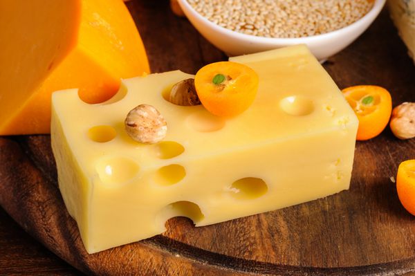 پنیرهای مختلف با آجیل و میوه در بشقاب چوبی
