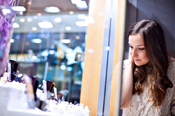 زن جوان زیبا از پشت شیشه در جواهر فروشی به نمایشگر نگاه می کند